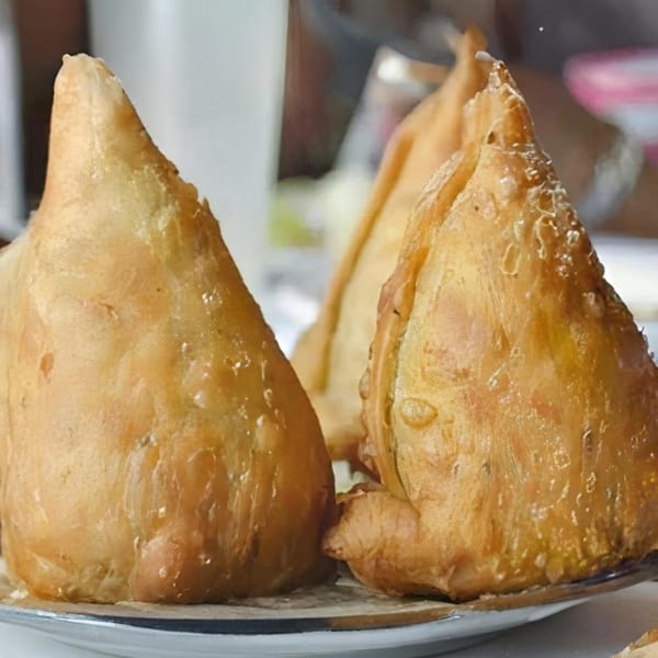 Three golden-brown, crispy Indian samosas, triangular in shape, arranged on a white plate.