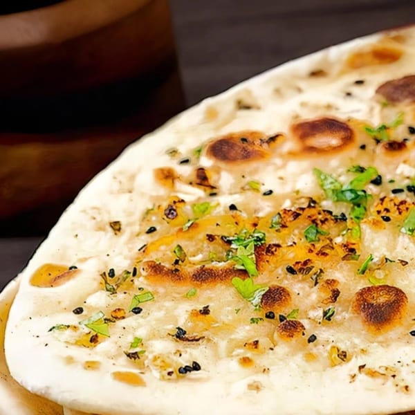 Close-up of Indian naan bread, garnished with fresh herbs and black sesame seeds.