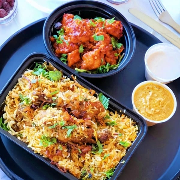 Tamarind Kitchen's Indian takeout meal with chicken biryani, chili chicken, and sauces on a black tray.