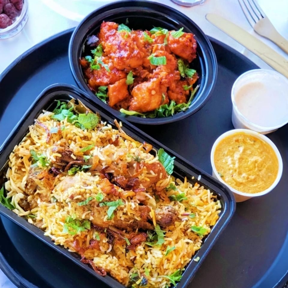 Tamarind Kitchen's Indian takeout meal with chicken biryani, chili chicken, and sauces on a black tray.