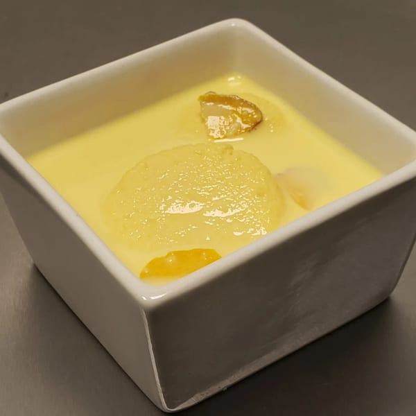Rasmalai, an Indian dessert, in a white square bowl with a creamy yellow sauce.