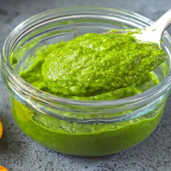 Bright green Indian chutney in a glass jar, with a spoon scooping some out.